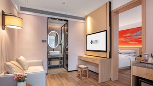 Ein modernes Hotelzimmer mit Holzboden, einer Couch, einem Schreibtisch, einem Bett, einem Fernseher und einem Badezimmer mit Spiegel und Waschbecken.