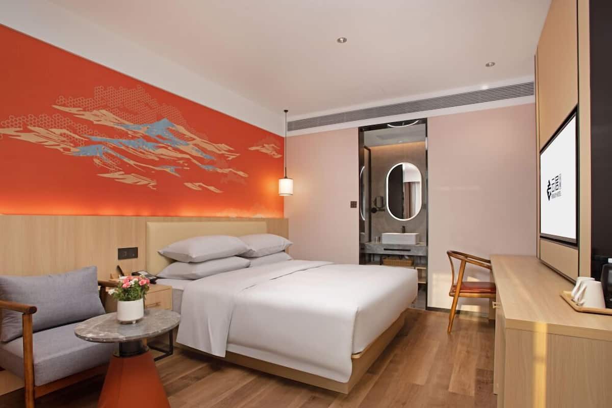 Ein modernes Hotelzimmer mit einem großen Bett, einer kleinen Couch, einem Schreibtisch und einem durchgegangenen Tür erkennbaren Badezimmer.