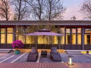 A traditional building with a tiled roof, a wooden fence, and a seating area with two lounge chairs and a table. - Yunju Hotel Beijing Yonghe Palace Guijie Siheyuan (Beijing)