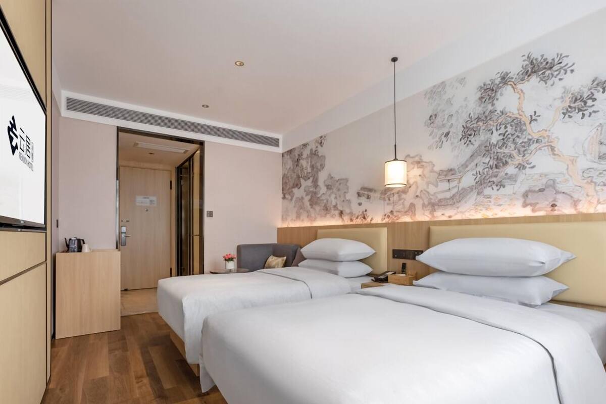 Ein Hotelzimmer mit zwei Betten, Holzboden, Wand mit einem Gemälde und einer Tür zu einem anderen Raum.