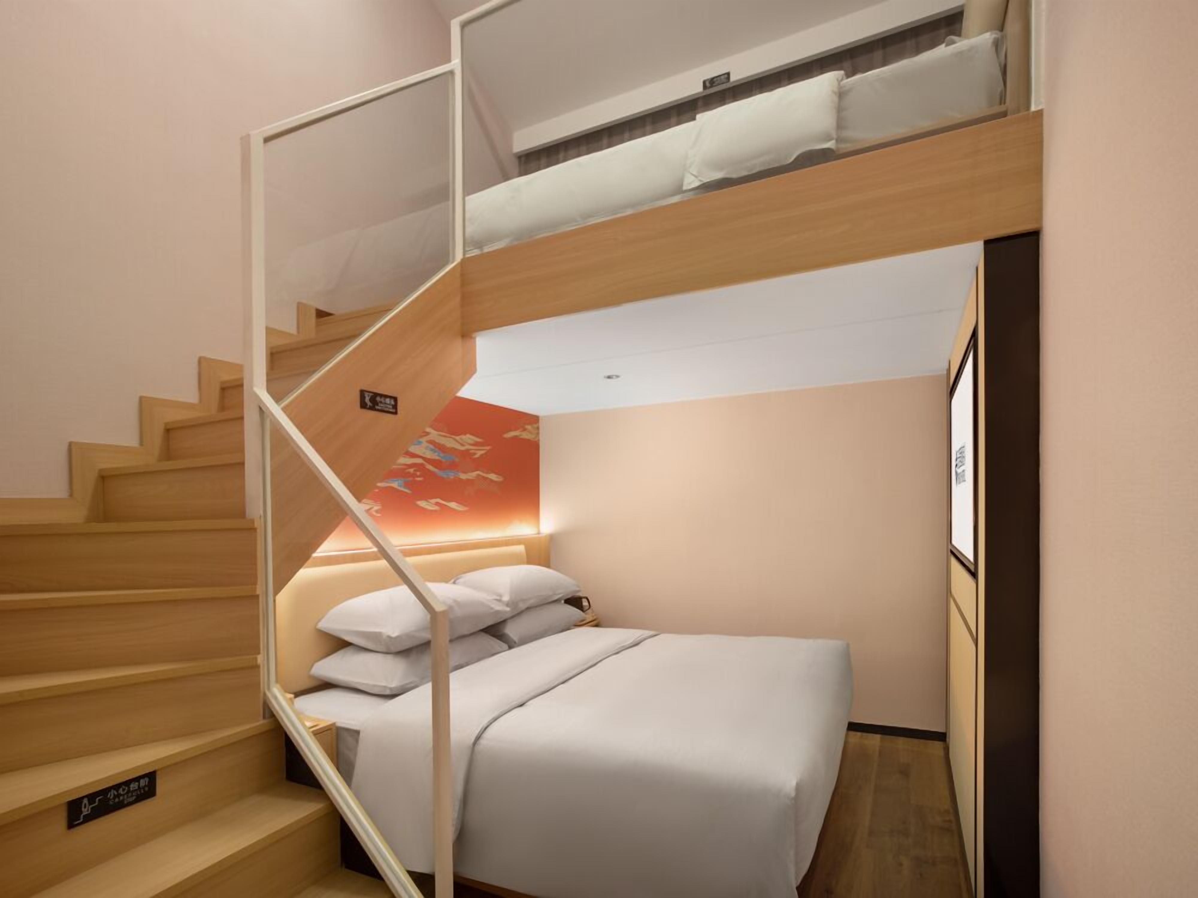 A compact hotel room with a bunk bed, a small desk, and a staircase.