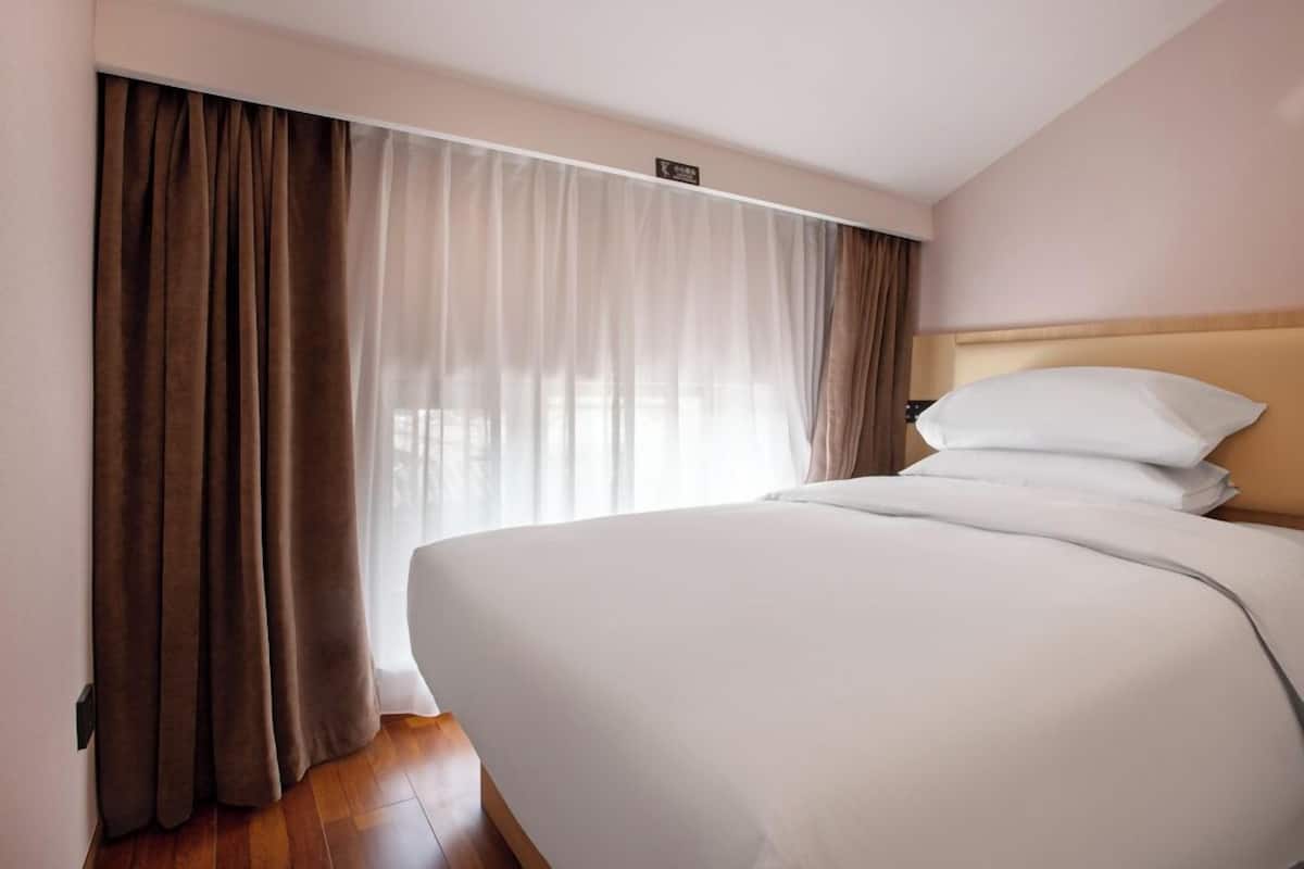 Ein Hotelzimmer mit einem großen Bett, einem Kopfteil und einem Fenster mit Vorhängen.