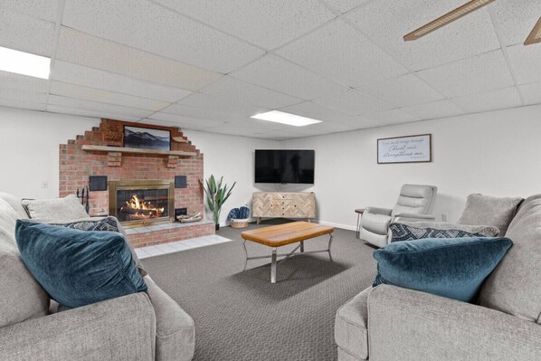 A living room with a brick fireplace, a flat-screen TV mounted on the wall, and a comfortable seating area with two sofas and a coffee table. - Riverfront, Hot Tub, Game Room, Camp Fire and More! (McVeytown)