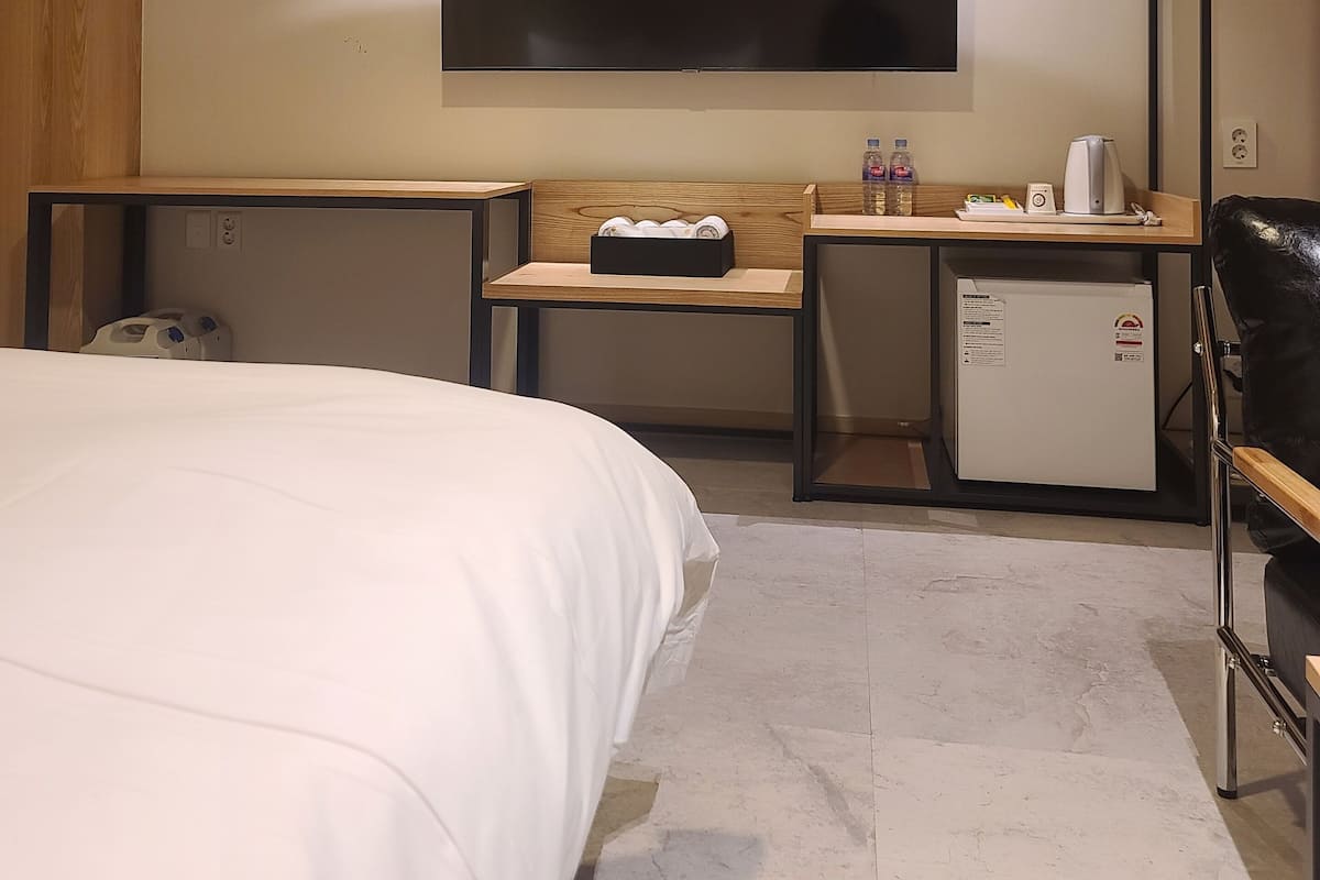 A hotel room with a bed, a desk, a chair, a flat-screen TV, and a mini-fridge.