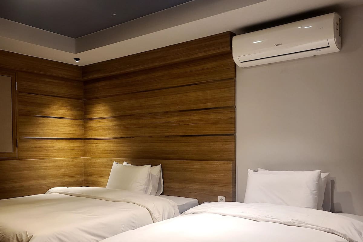 A hotel room with two beds, wooden paneling on the walls, and an air conditioning unit mounted on the wall.