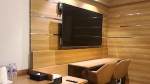 Een moderne hotelkamer met een houten wandpaneel, een flatscreen televisie boven een houten bureau, een koffiezetapparaat en twee stoelen.