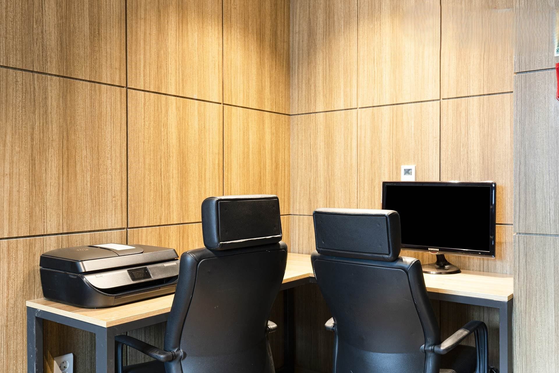 Une pièce comprenant deux chaises de bureau noires, un bureau, une imprimante et un écran d’ordinateur.