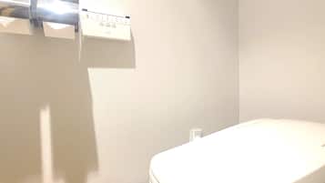 A bathroom with a toilet, a trash bin, and a paper towel dispenser on the wall.