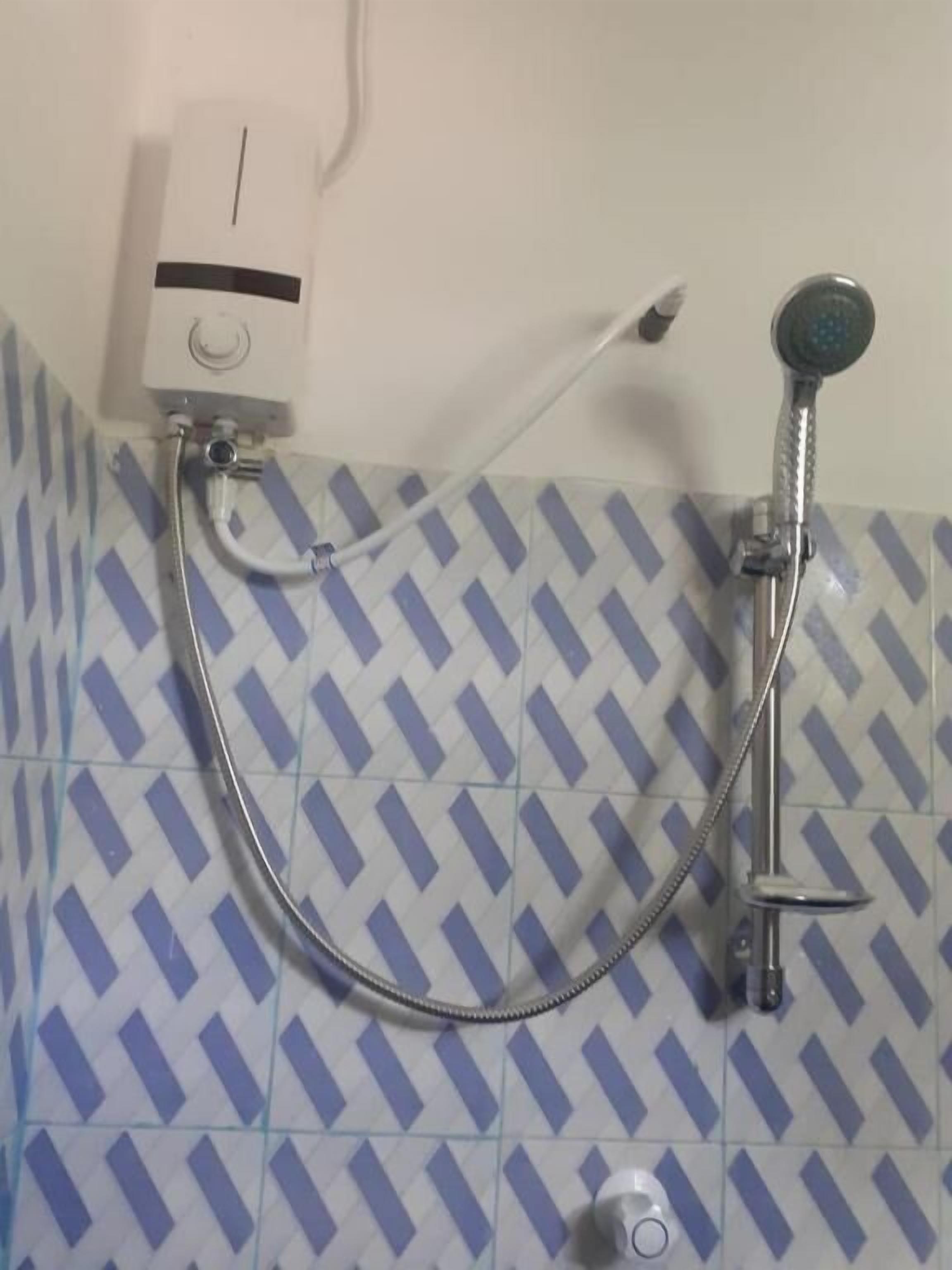 A shower with a handheld hose and a wall-mounted showerhead, connected to a wall-mounted control panel.