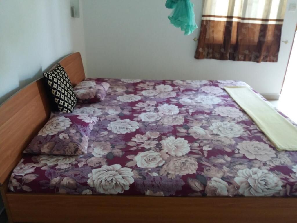 Uma cama com colcha florida, cabeceira de madeira e travesseiro estampado.