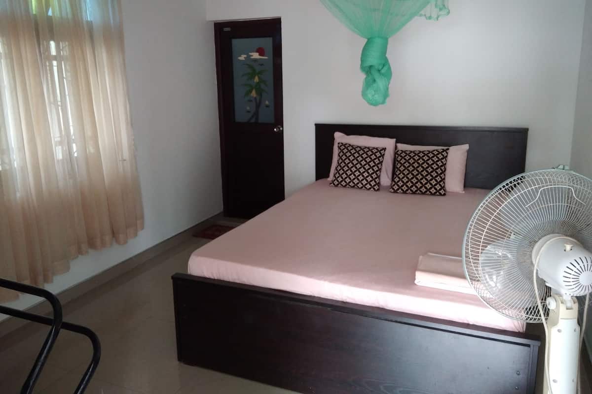 Un dormitorio con cama, ventilador, puerta con ventana y cortina.