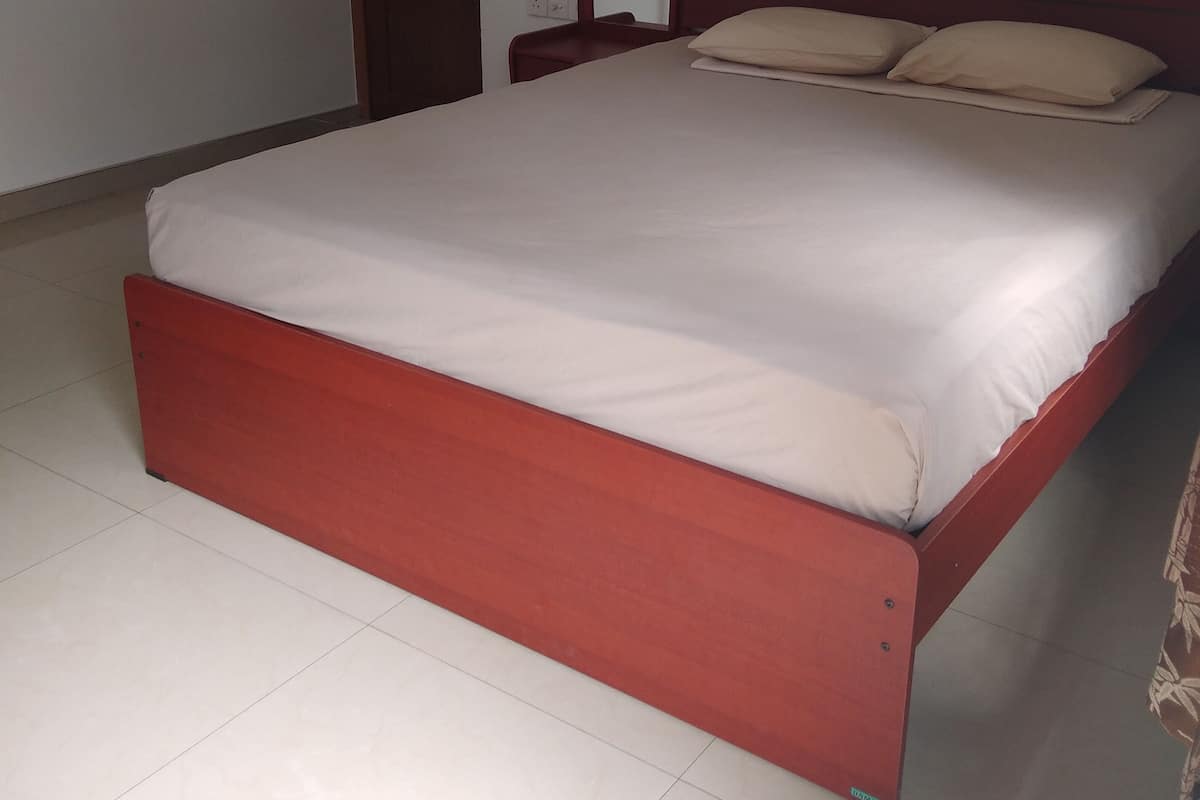 Habitación individual con una cama de madera, ropa de cama blanca y una cortina verde.