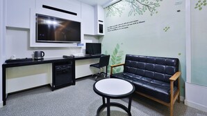 A modern room with a black leather sofa, a small round table, a TV mounted on the wall, a desk with a computer, and a microwave. - G&G Hotel (Ulsan)