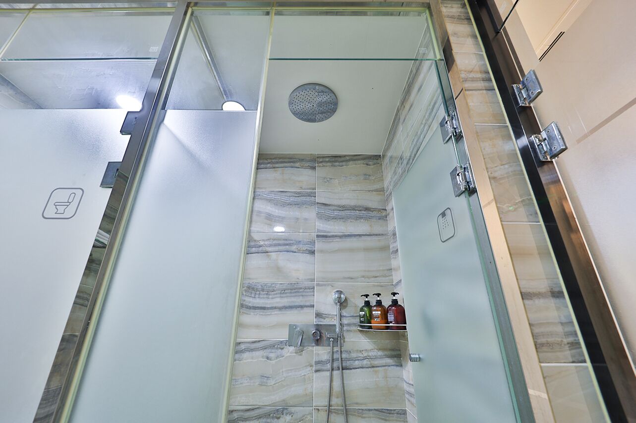 Un baño moderno con cabina de ducha de vidrio, baldosas de mármol y estante empotrado con artículos de aseo.