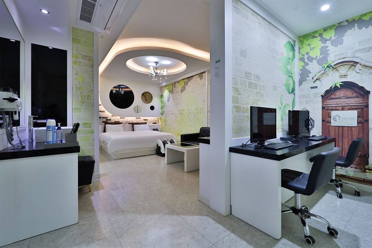 A modern hotel room with a bed, desk, and computer setup.