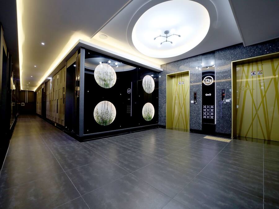 Un pasillo moderno de hotel con piso oscuro, decoraciones circulares en la pared y dos ascensores.