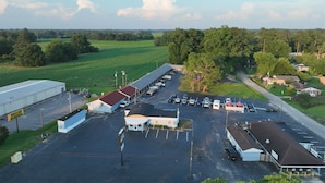 An aerial view of a parking lot with several buildings, including a large warehouse and a smaller structure with a red roof. - Imperial Motel (Mullins)