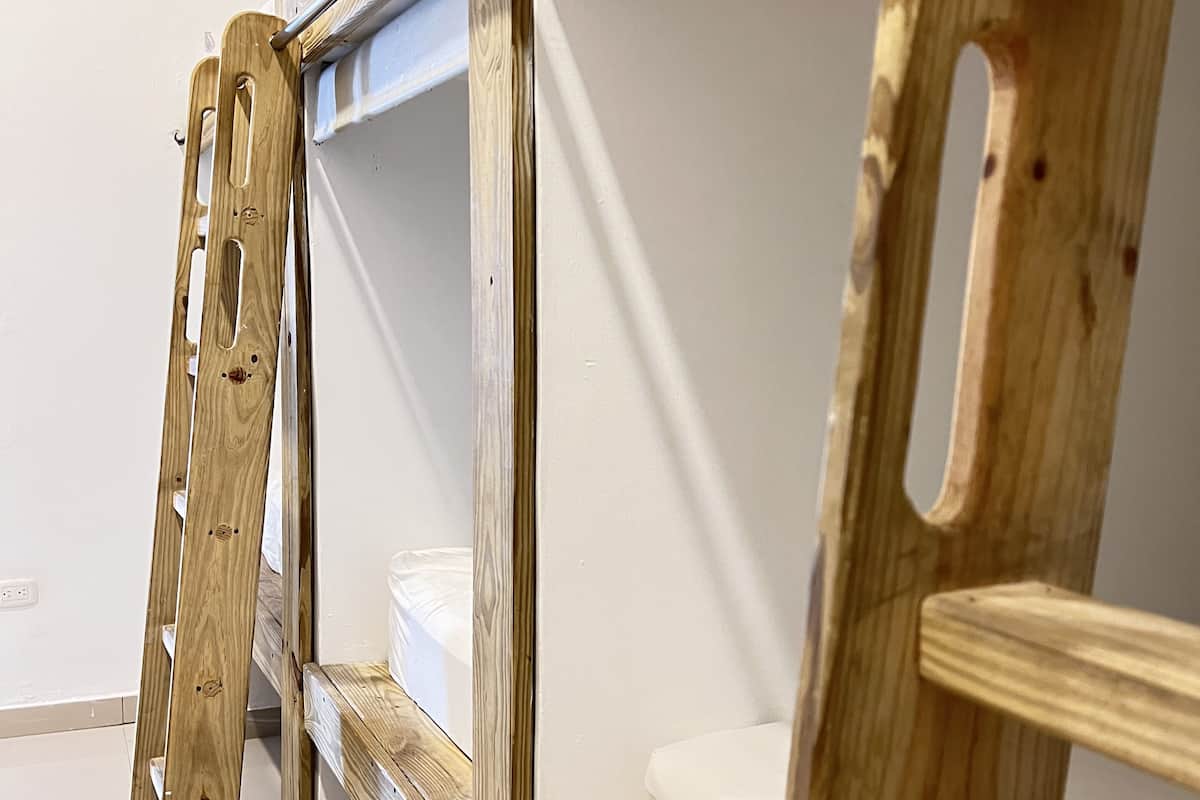Ein Etagenbett mit Metallgestell und Holzleisten, eine weiße Wand und ein gefliester Boden.