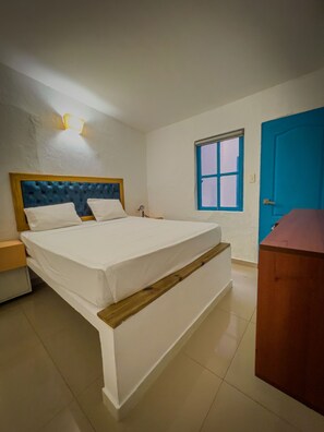 Une chambre à coucher comprenant un lit, une table de chevet, une commode, une fenêtre avec des stores et une porte.