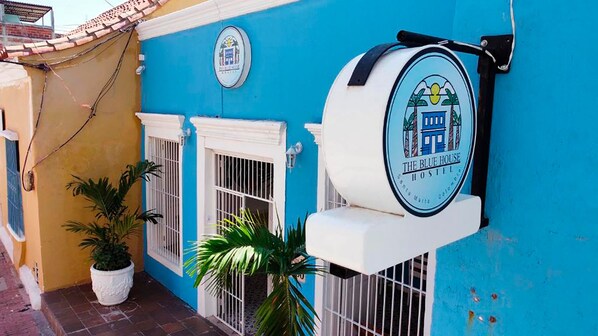 Une enseigne d’auberge aux couleurs bleu et blanc, avec un logo et le nom « The Blue House Hostel ».
