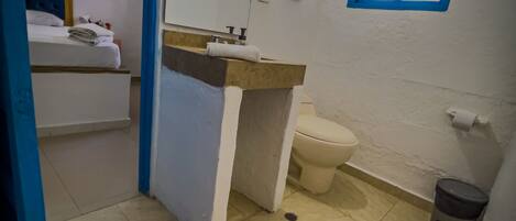 A small bathroom with a toilet, sink, and a mirror. There is a blue-framed window and a sign on the wall.