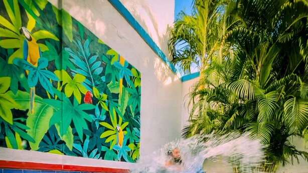 Une piscine ornée d’une fresque aux motifs tropicaux et bordée de palmiers.