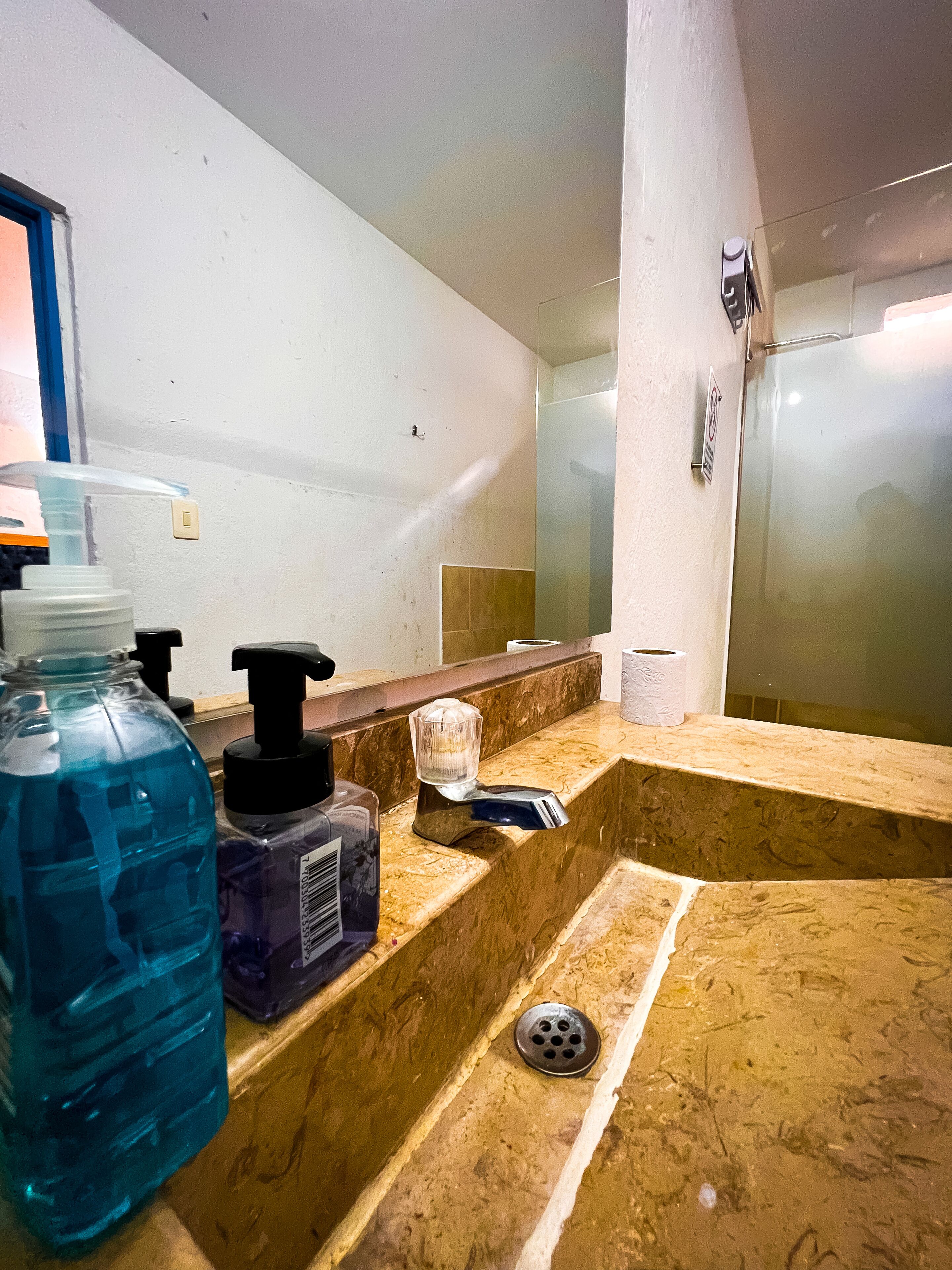 A bathroom with a marble sink, a large blue water bottle, a hand soap dispenser, and a toilet paper roll.
