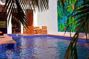 Une piscine dotée de chaises longues en bois et ornée d’une fresque murale aux couleurs vives.