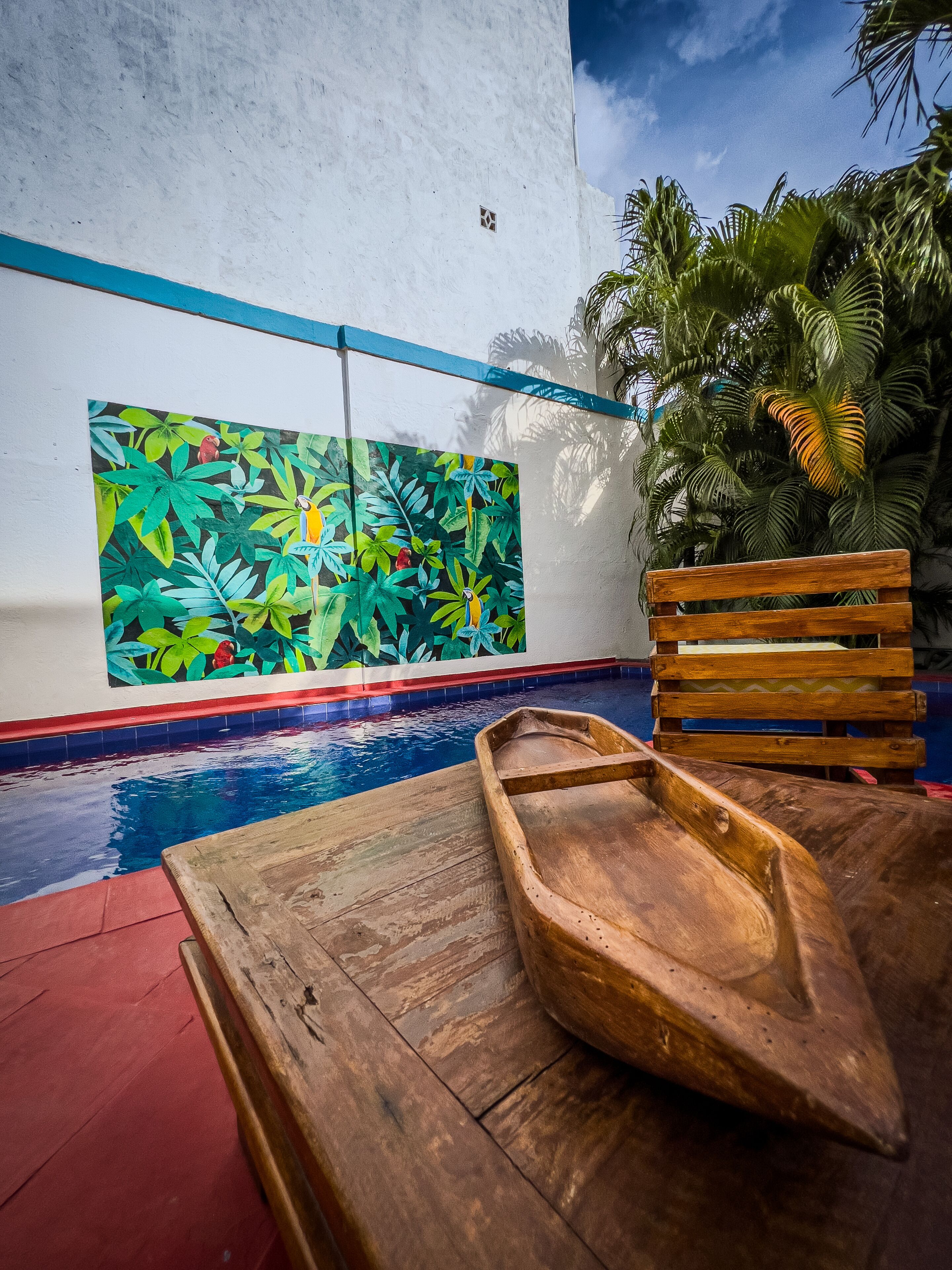 A wooden boat by a pool with a mural of tropical foliage and birds.