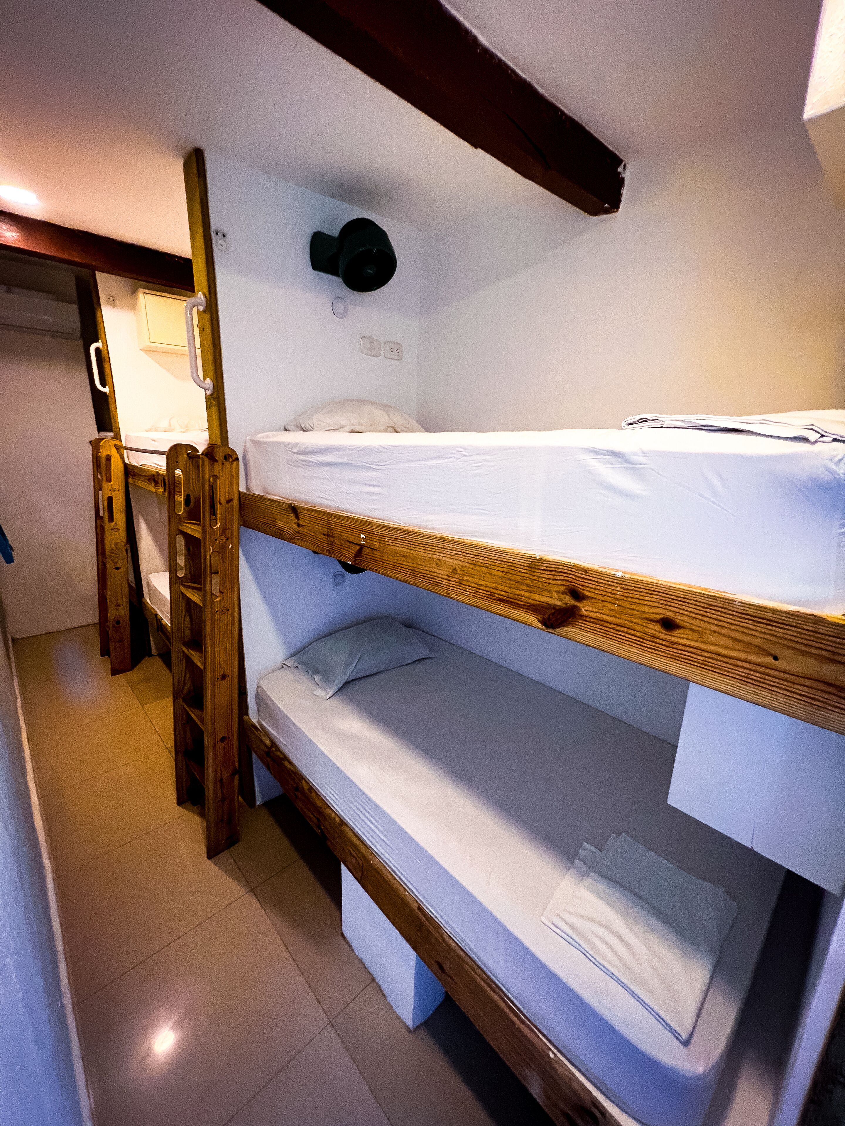 Habitación con literas, una escalera de madera, un escritorio pequeño y un espejo en la pared.