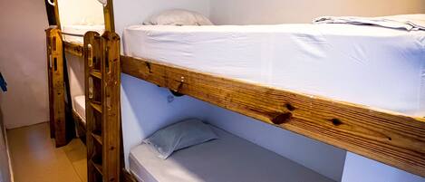 Habitación con literas, una escalera de madera, un escritorio pequeño y un espejo en la pared.