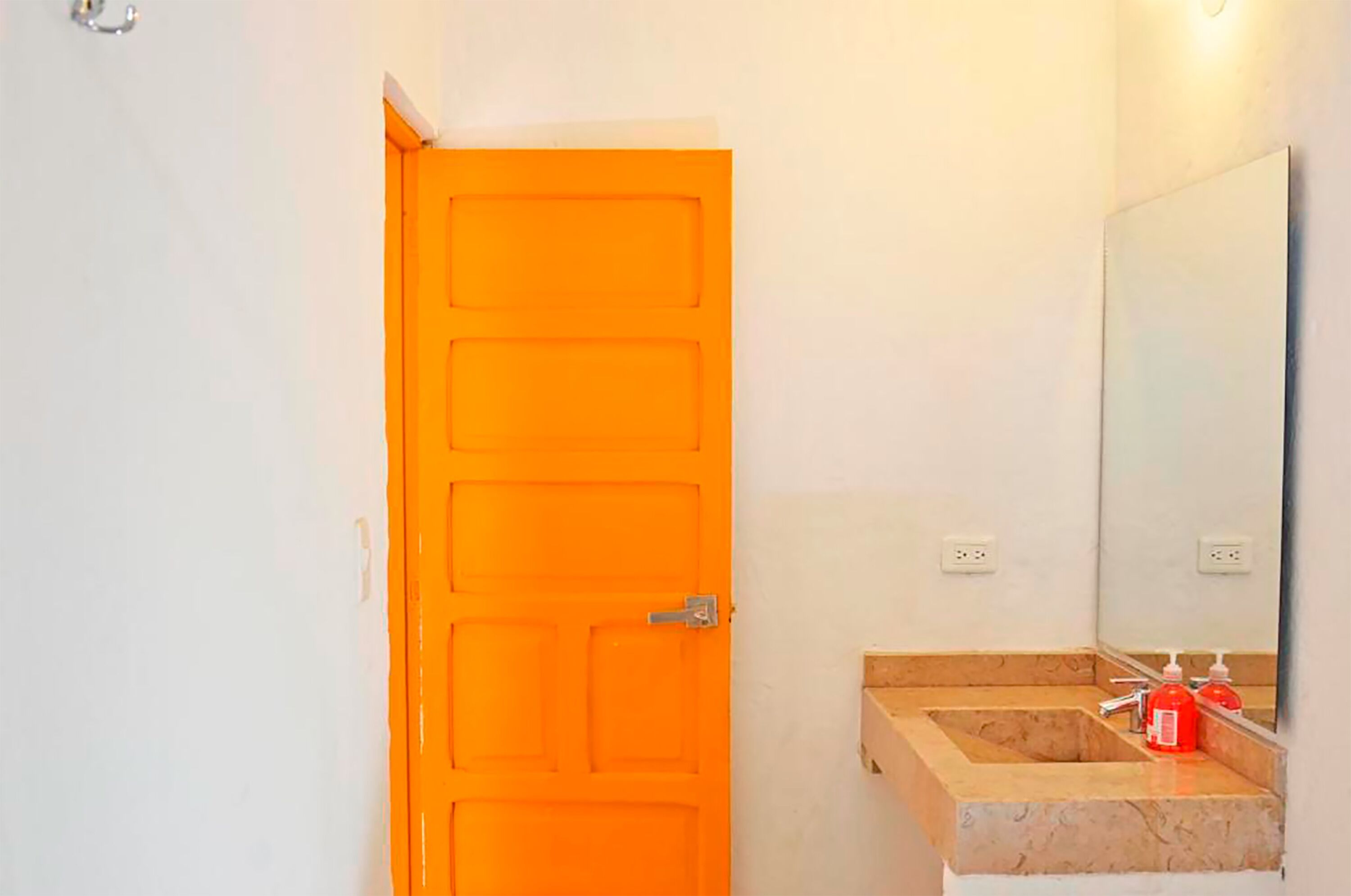 A bathroom with an orange door, a sink with a marble countertop, and a mirror above it.