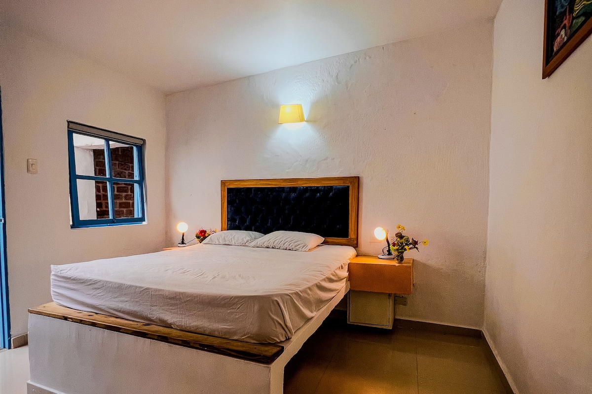 Ein Schlafzimmer mit Bett, Nachttisch, Wandlampe, Fenster und einem Bild an der Wand.