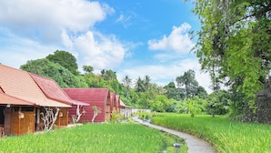 A traditional red-roofed building with a pathway leading through a lush green rice field. - Uma Raos Cottage (Ubud)