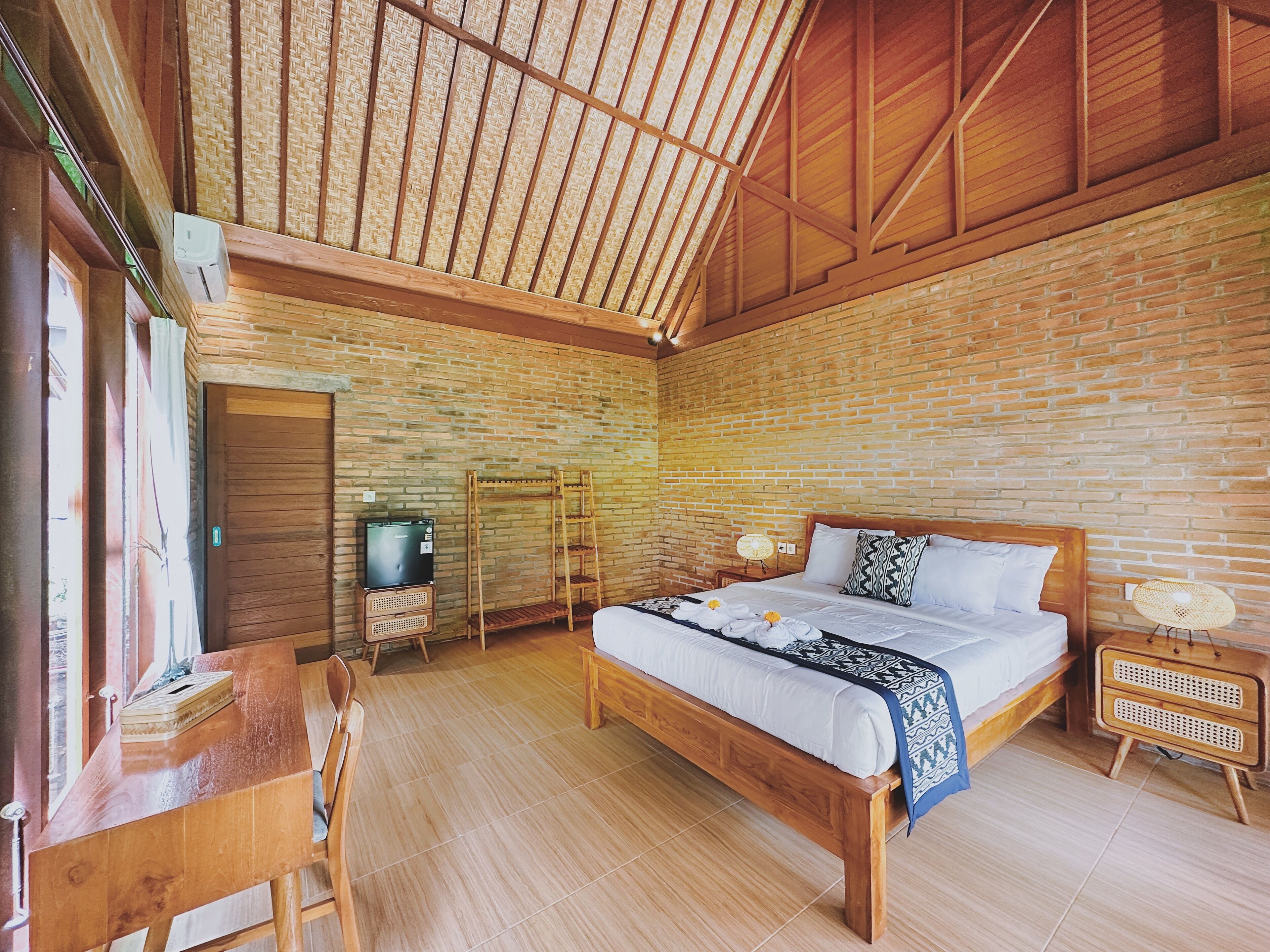 A bedroom with a wooden bed, a desk, a chair, a TV, and a shelf.