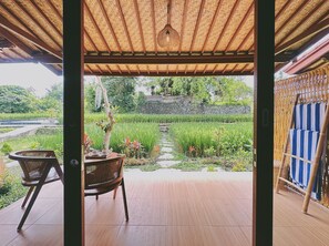 Ein überdachter Außenbereich mit Blick auf einen Garten und Reisfelder.