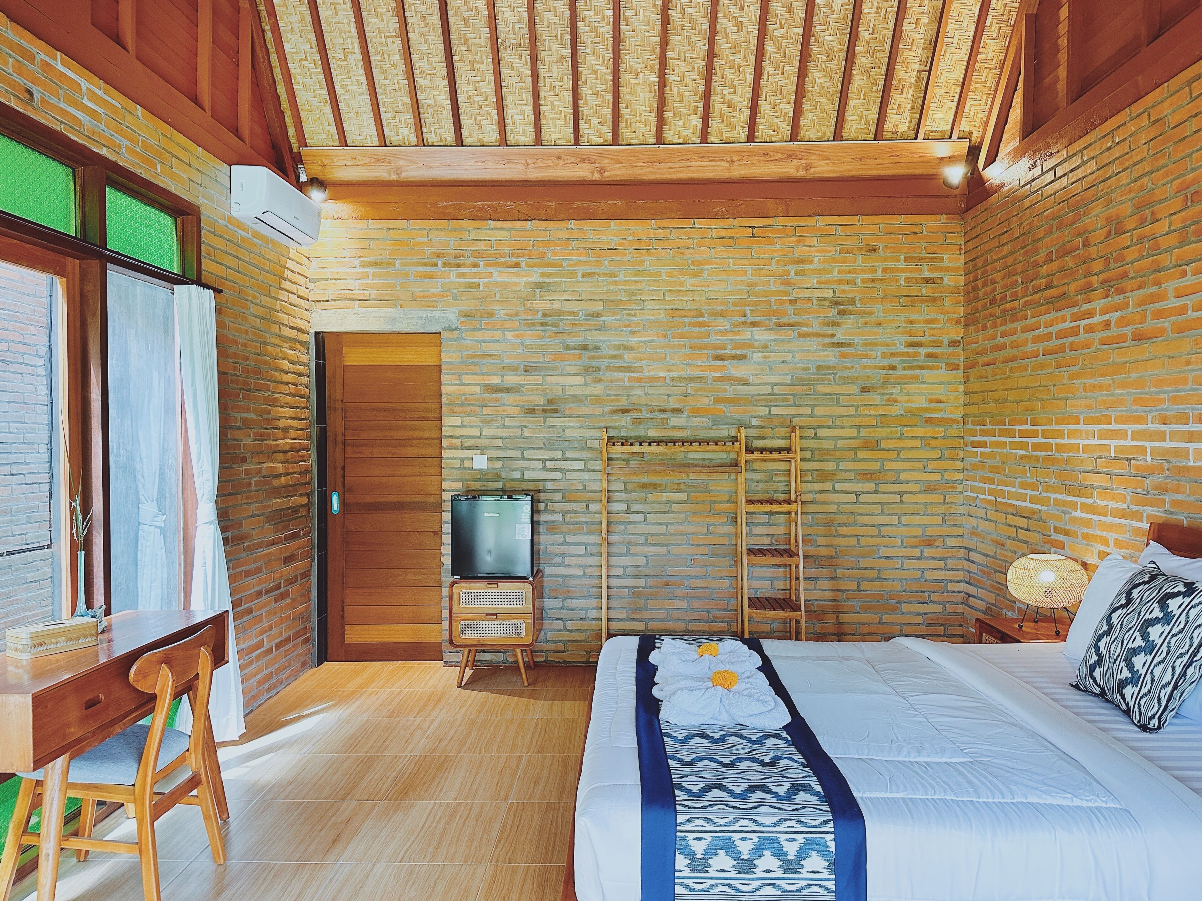 Una habitación con pared de ladrillo, un escritorio de madera, una cama con colcha estampada y techo de vigas de madera.