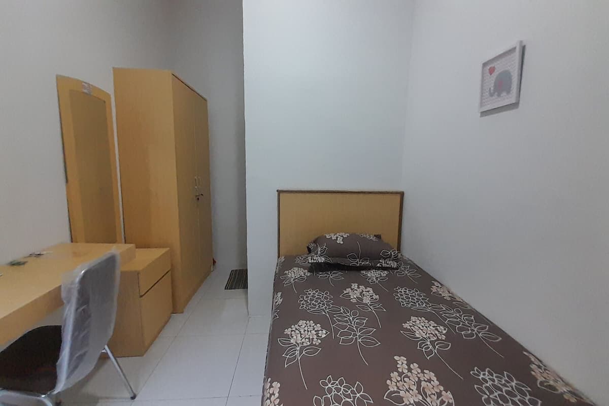 A small, neatly arranged bedroom with a single bed, a desk, and a chair.