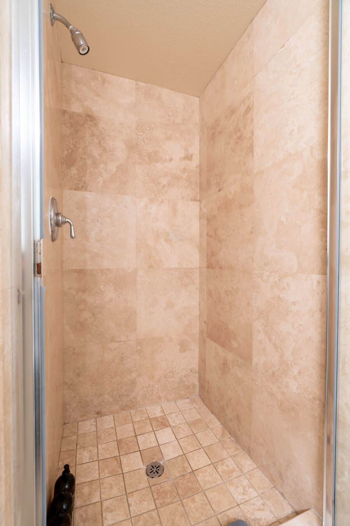 A small, enclosed shower area with beige tiles and a drain in the center.