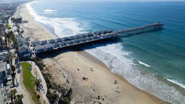Une plage avec une longue jetée qui s’avance dans l’océan, entourée d’immeubles d’habitation.