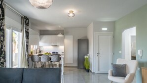 A modern living room with a grey sofa, a white armchair, and a dining area with a kitchen in the background. - Nisimos Modern Apartment (Hersonissos)