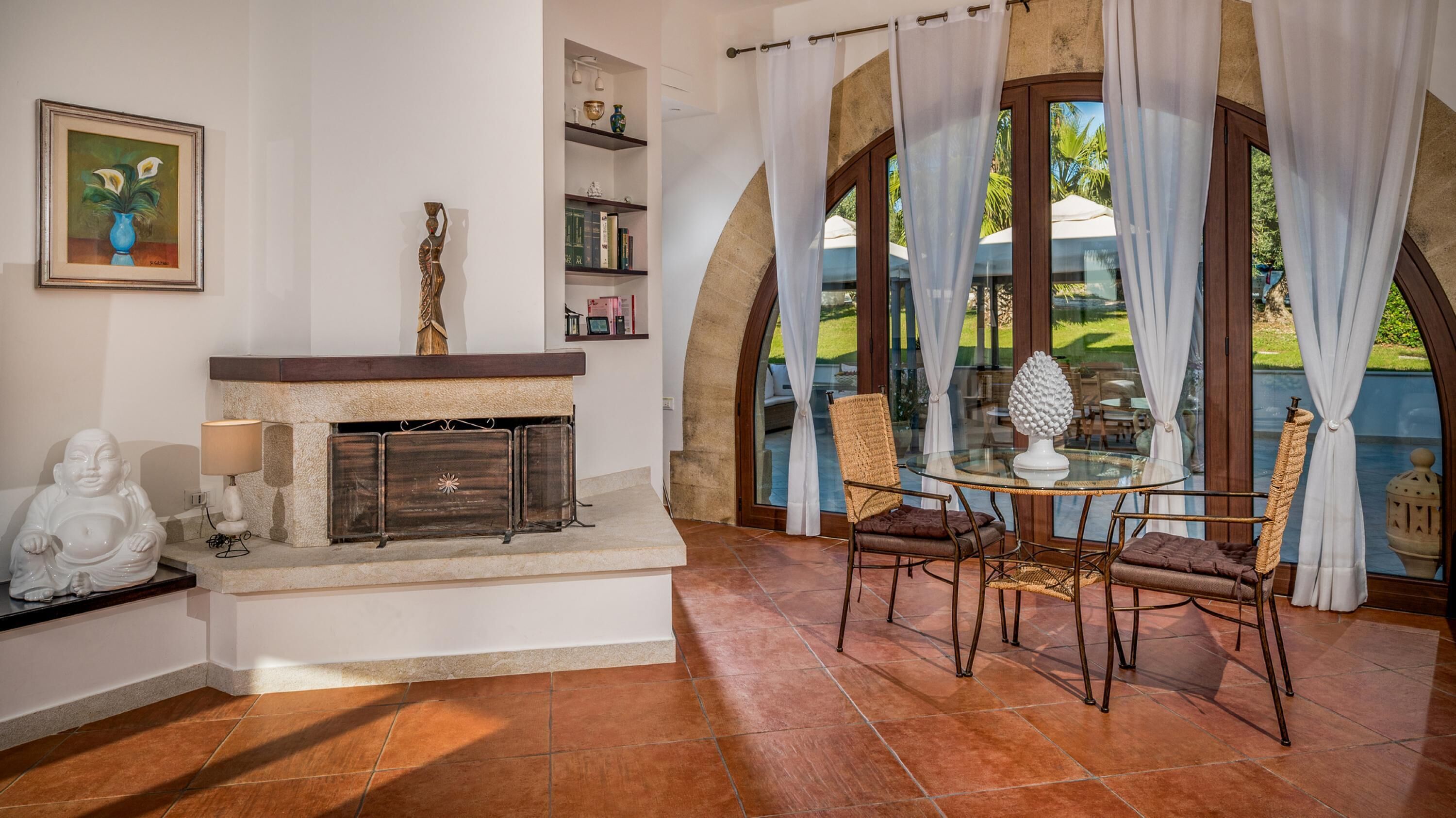 A cozy living room with a fireplace, a dining area with a glass table, and a view of a garden through large windows.