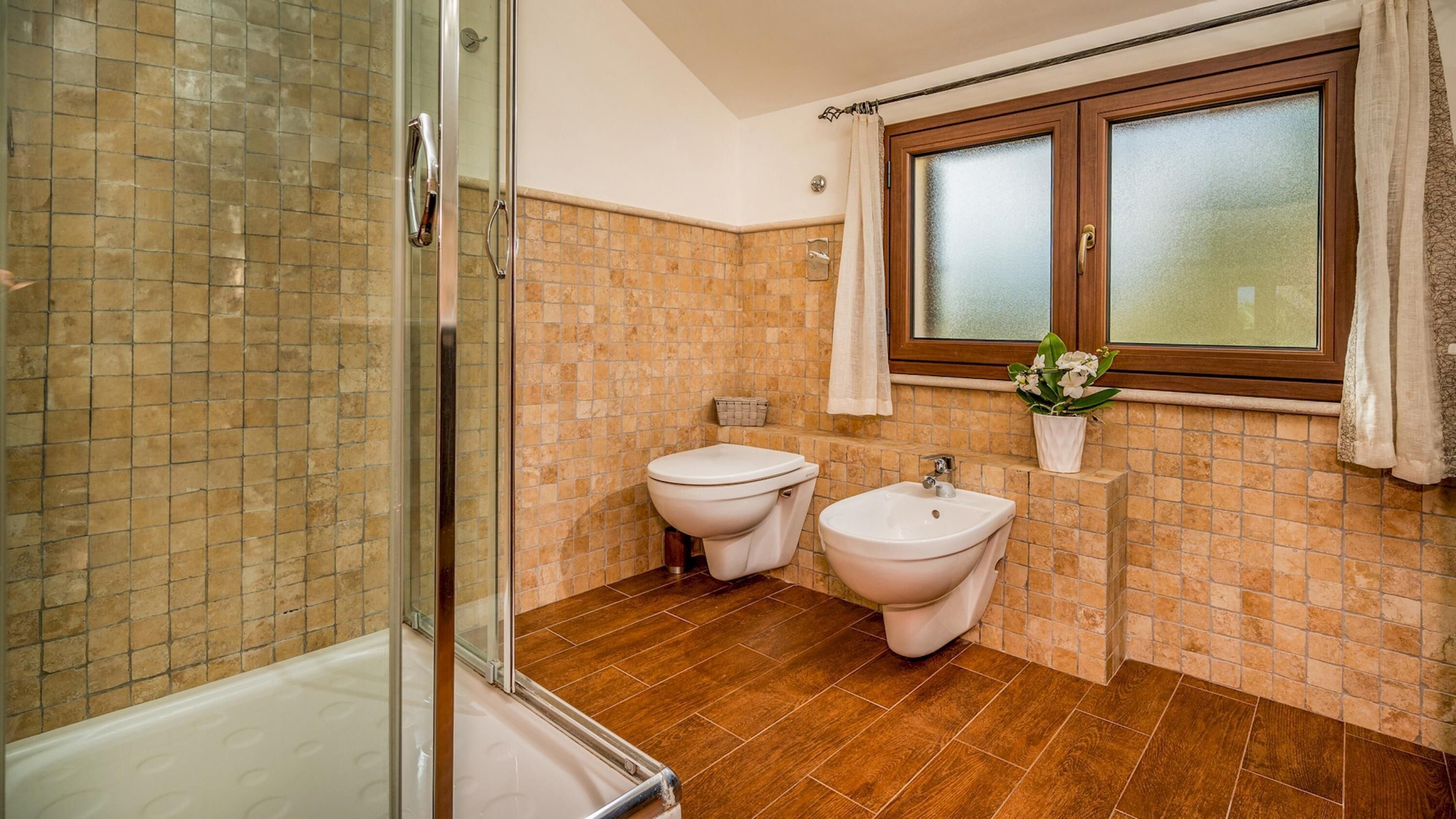 A bathroom with a glass shower enclosure, two toilets, a bidet, and a sink.