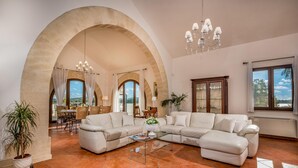 A spacious living room with a large arched doorway, a chandelier, and a view of the outdoors. - Villa Donna Agaver 6 Emma Villas (Paceco)