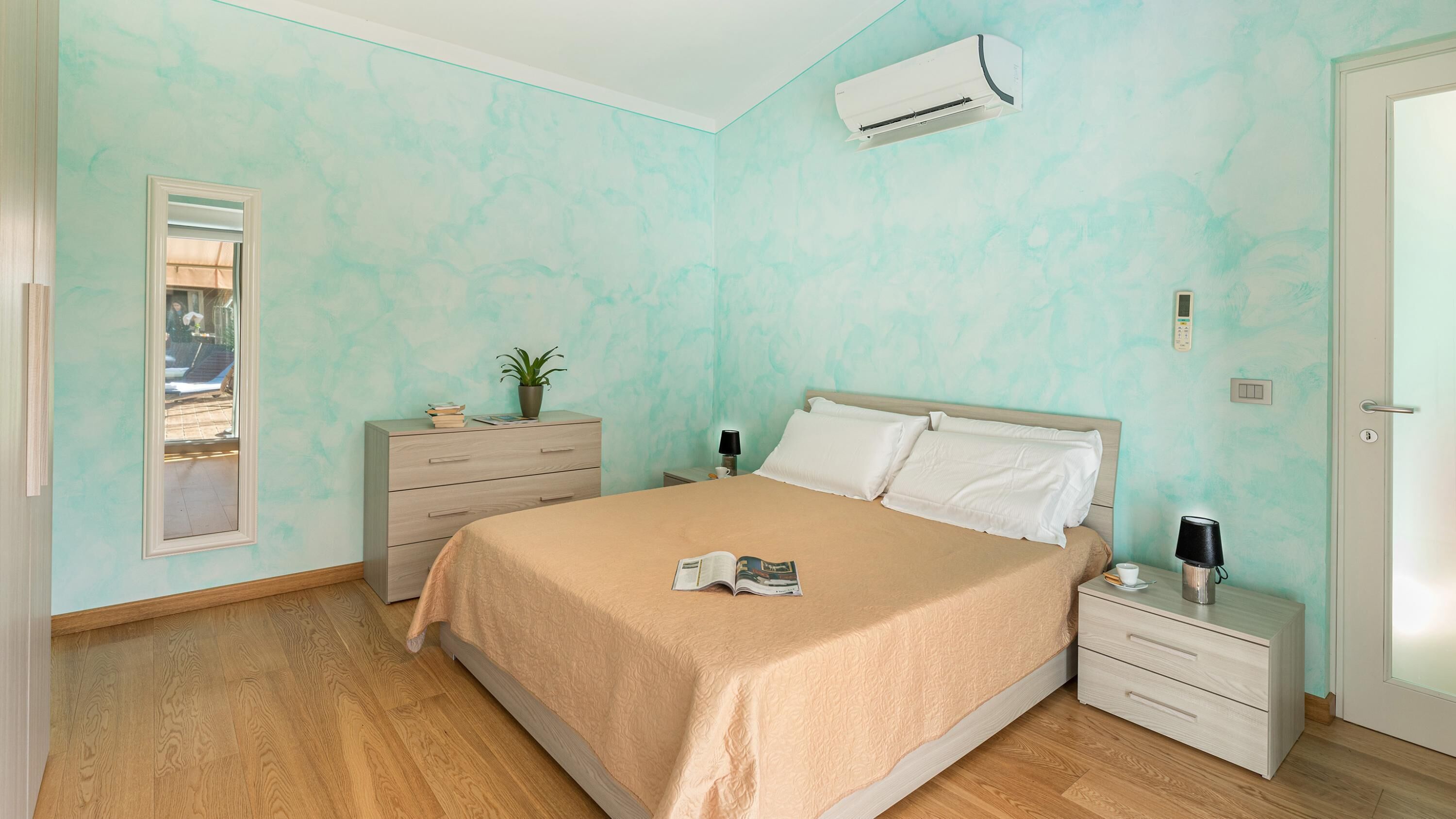 A bedroom with a bed, bedside tables, a nightstand, a mirror, and an air conditioning unit.