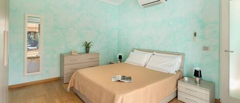 A bedroom with a bed, bedside tables, a nightstand, a mirror, and an air conditioning unit.