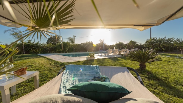 A sunlit outdoor relaxation area with a pool, lounge chairs, and a covered seating area. - Profumo di Zagara 6 2 Emma Villas (Ispica)