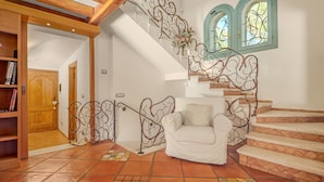 Un escalier orné de rampes en métal, un fauteuil blanc et une bibliothèque en bois.