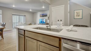 A modern kitchen with a large island, stainless steel appliances, and a dining area with a wooden table and chairs. - Top Flight (Colorado Springs)
