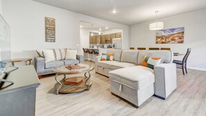 A modern living room with a grey sectional sofa, a round coffee table, and a dining area with a white table and chairs. - Top Flight (Colorado Springs)